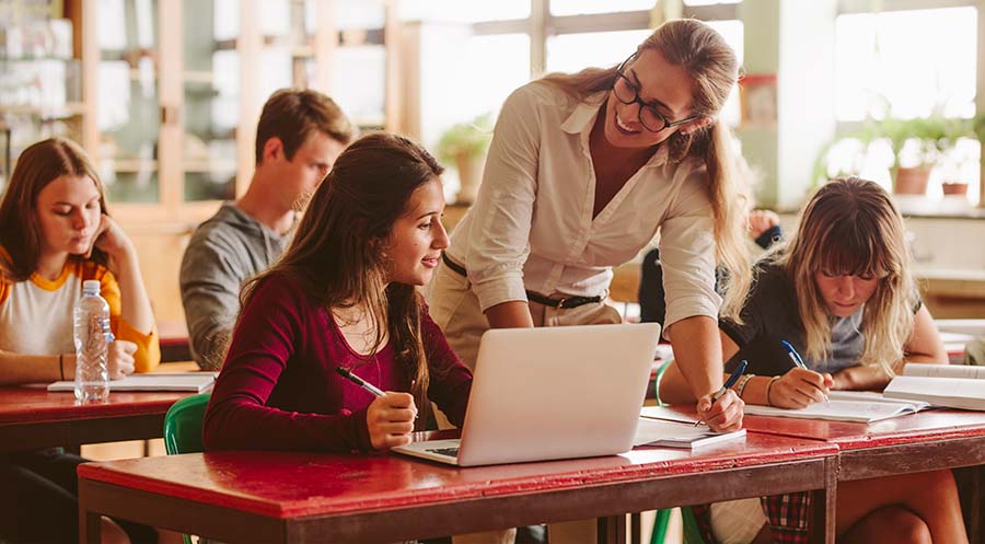 a teacher standing over a student at a laptop