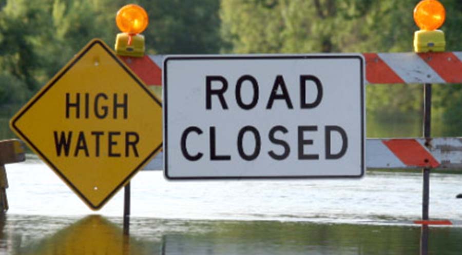 Road closed due to flooding sign sitting in water.